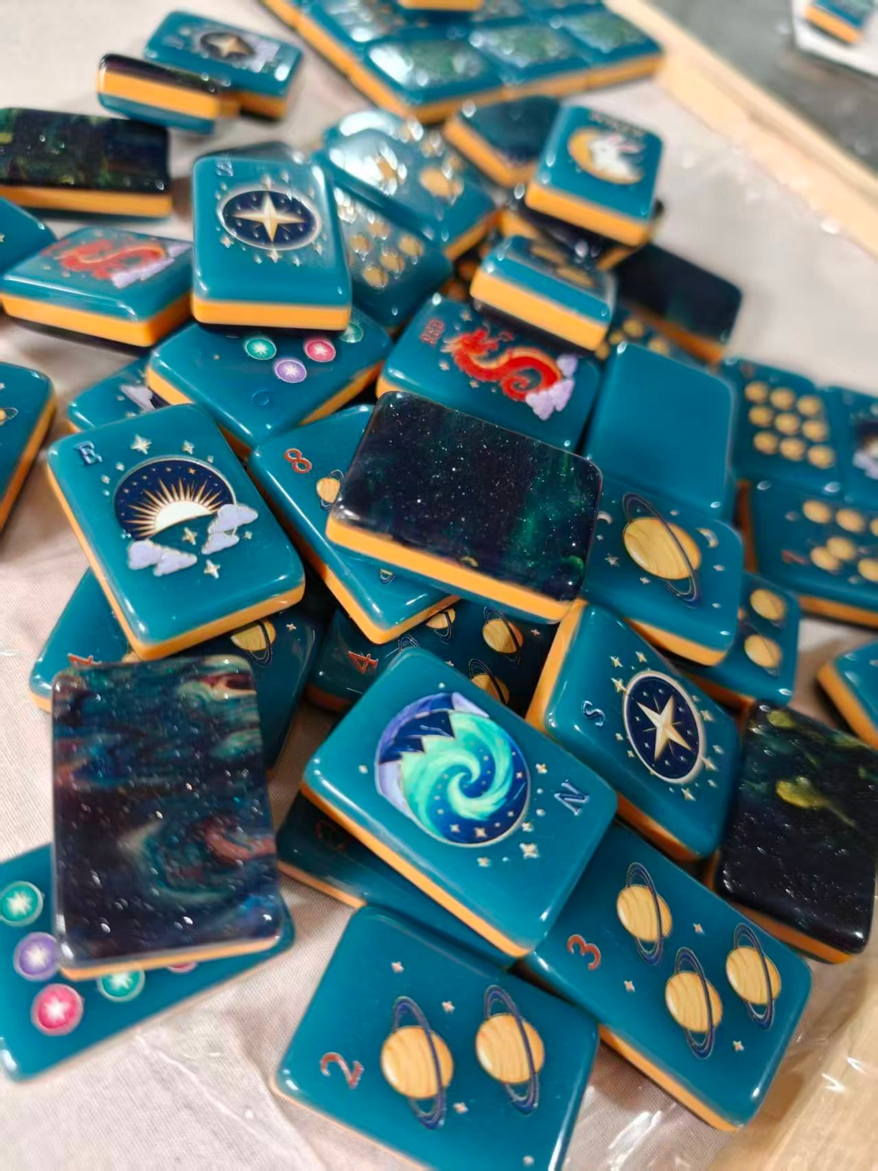 Midnight Galaxy tiles in a pile — teal faces, amber sides, galaxy backs